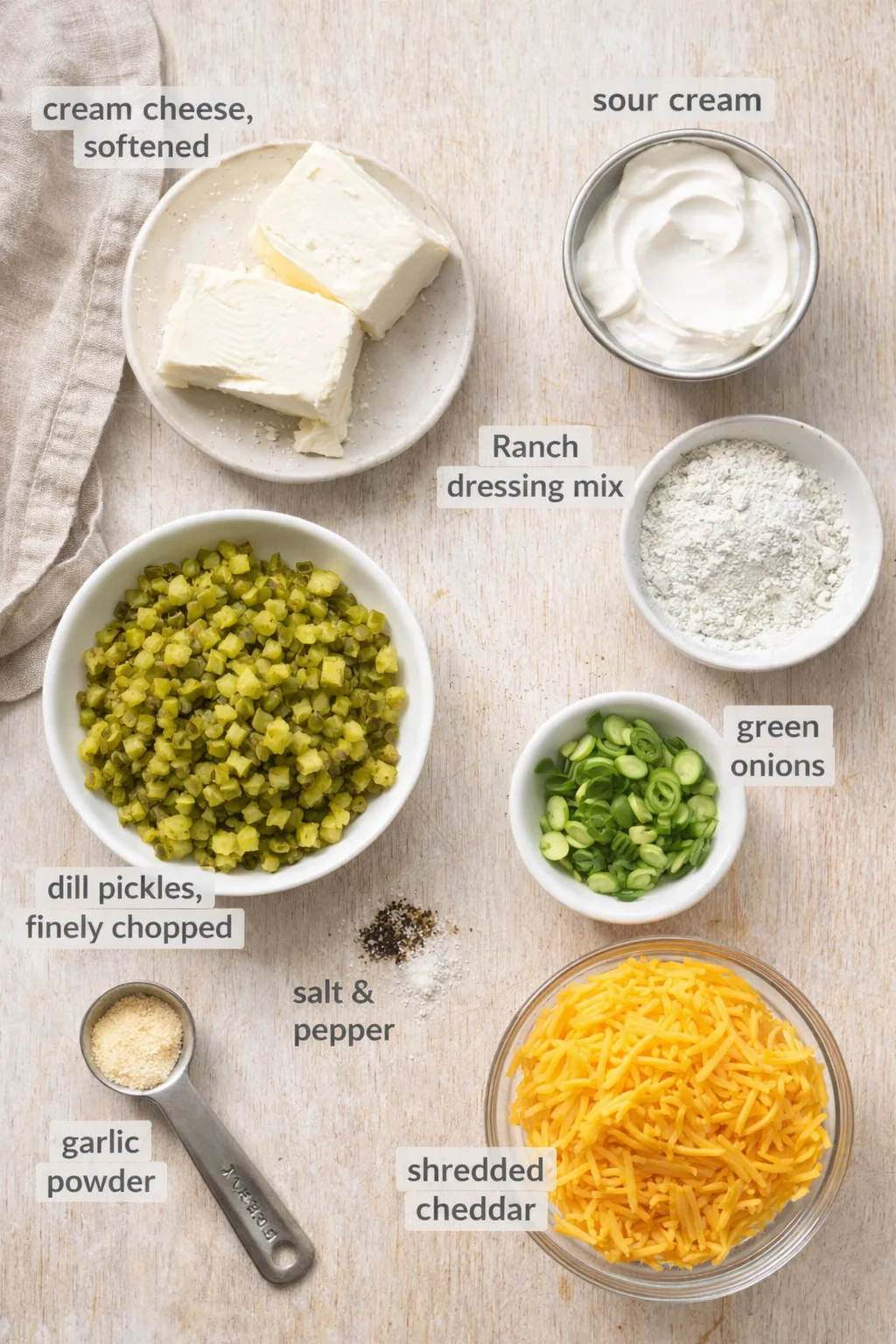 Flat lay of ranch dip ingredients on a light wood background with items like cream cheese, sour cream, and cheddar.