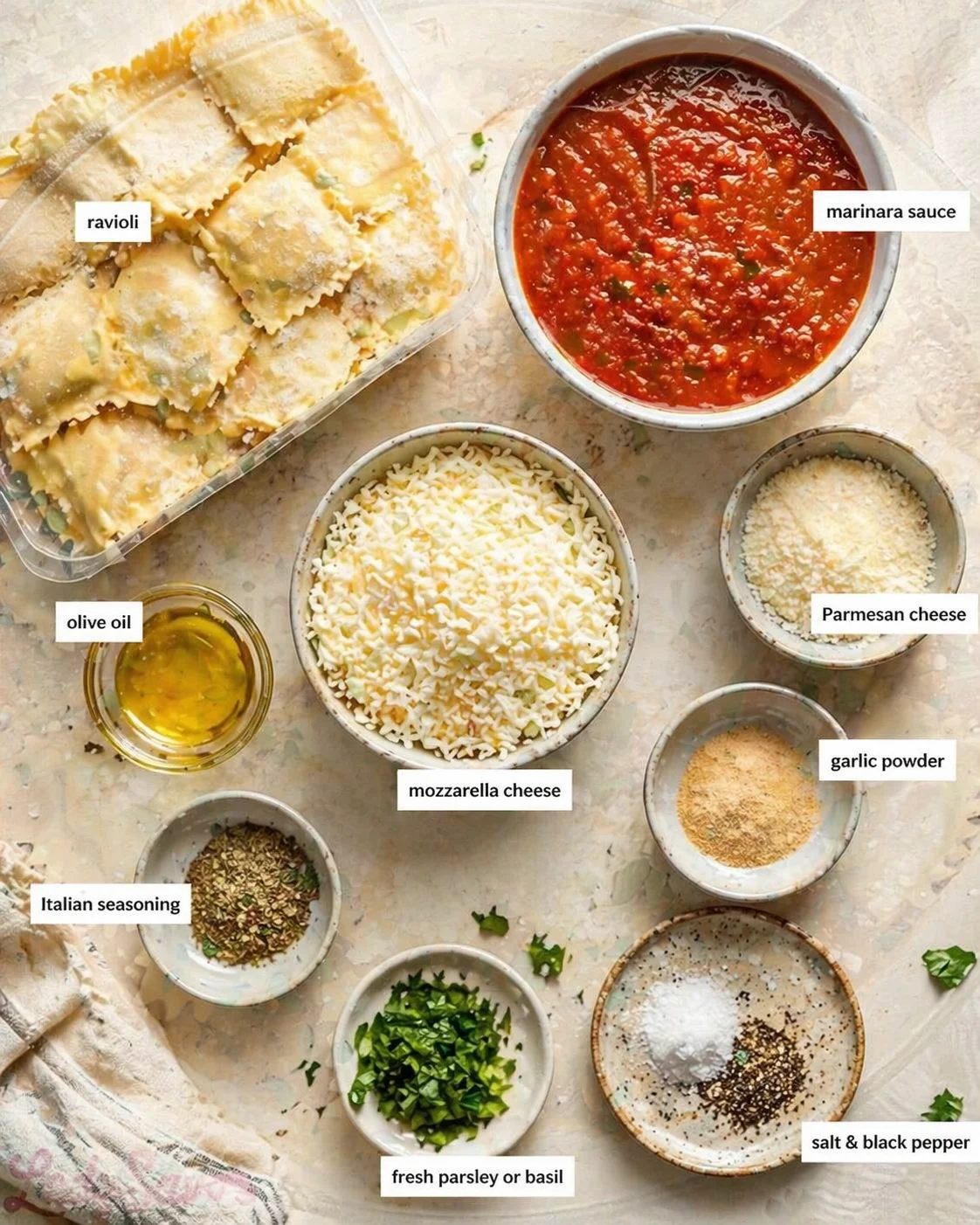 Overhead shot of labeled ravioli ingredients arranged on a marble counter: sauce, cheeses, oil, herbs.