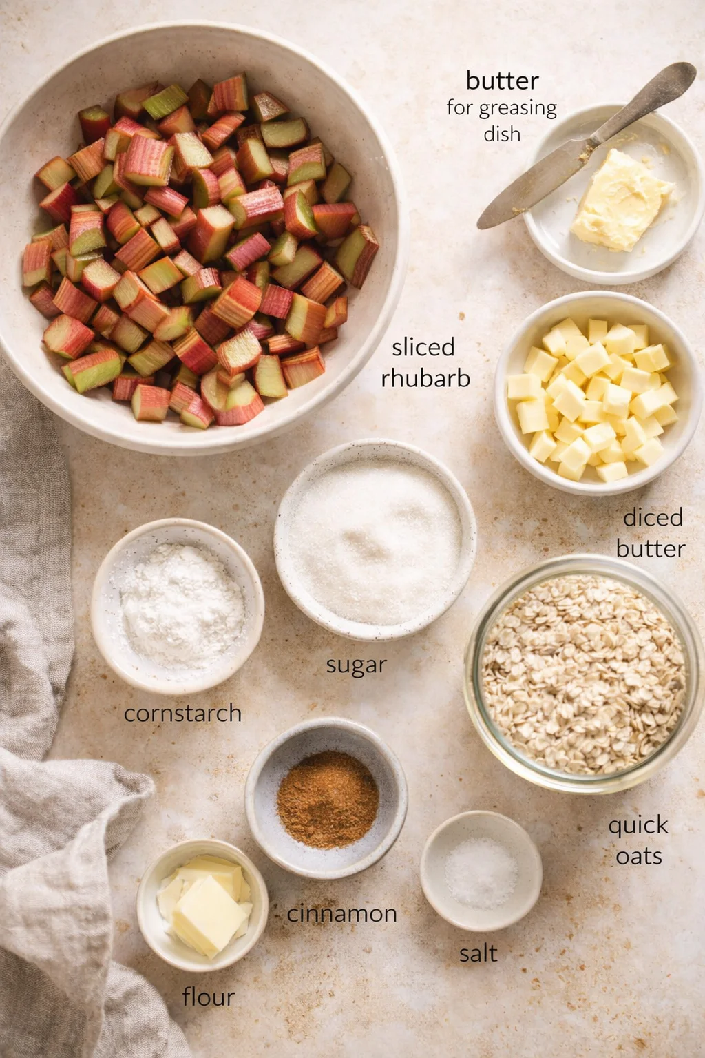 top-down view of rhubarb cubes and baking ingredients in bowls on a beige countertop for a crumble recipe with labeled text