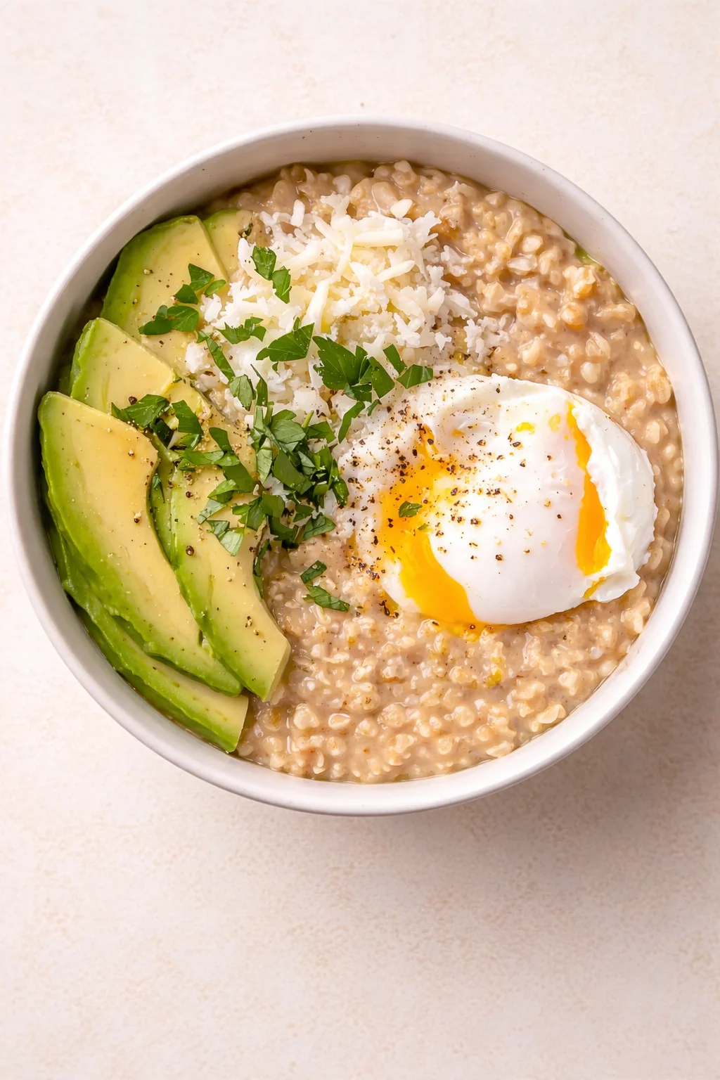 Top-down view of a bowl of savory oatmeal with avocado, egg, cheese, and herbs.