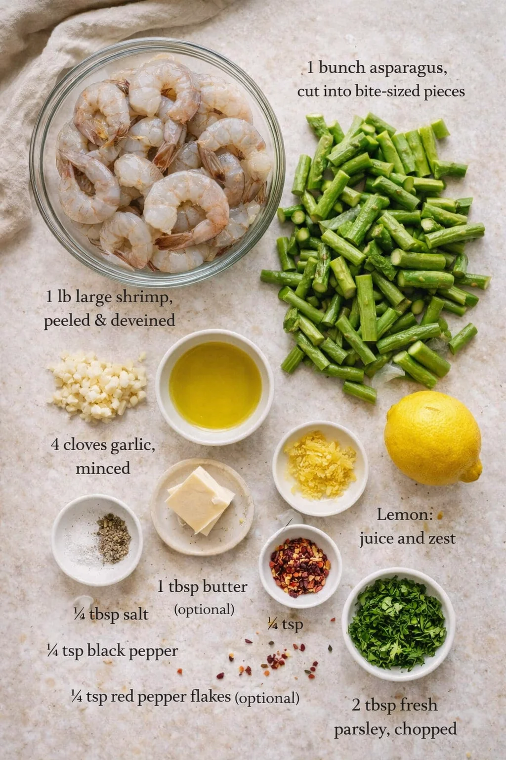 top-down layout of raw ingredients: shrimp, asparagus, lemon, garlic, butter, and oil labeled on a beige surface.