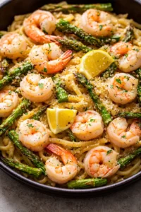 plated shrimp and asparagus pasta with lemon wedges and parmesan in a skillet