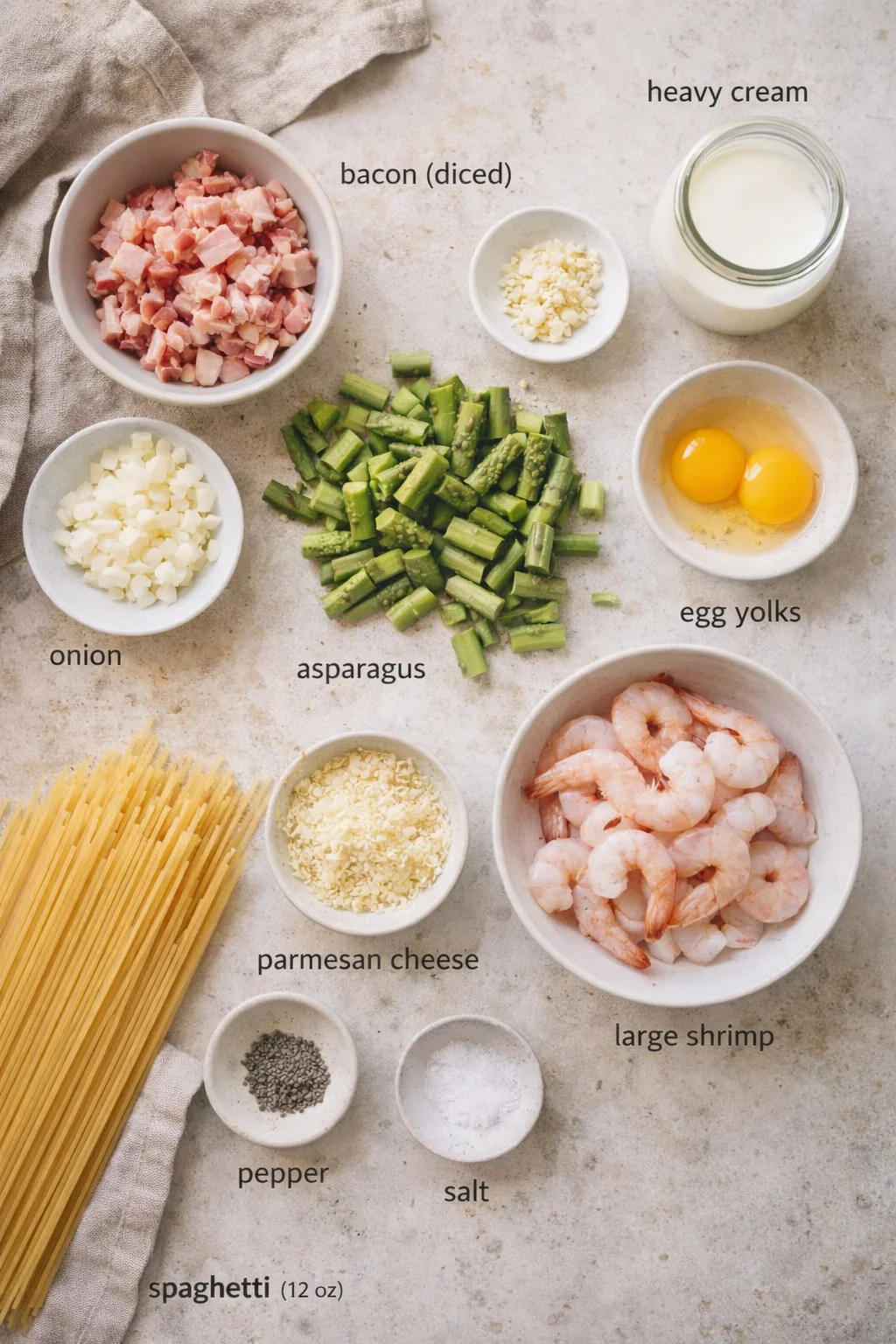 Overhead shot of labeled ingredients for shrimp pasta, including bacon, asparagus, shrimp, eggs, cream, garlic, cheese, and spaghetti.