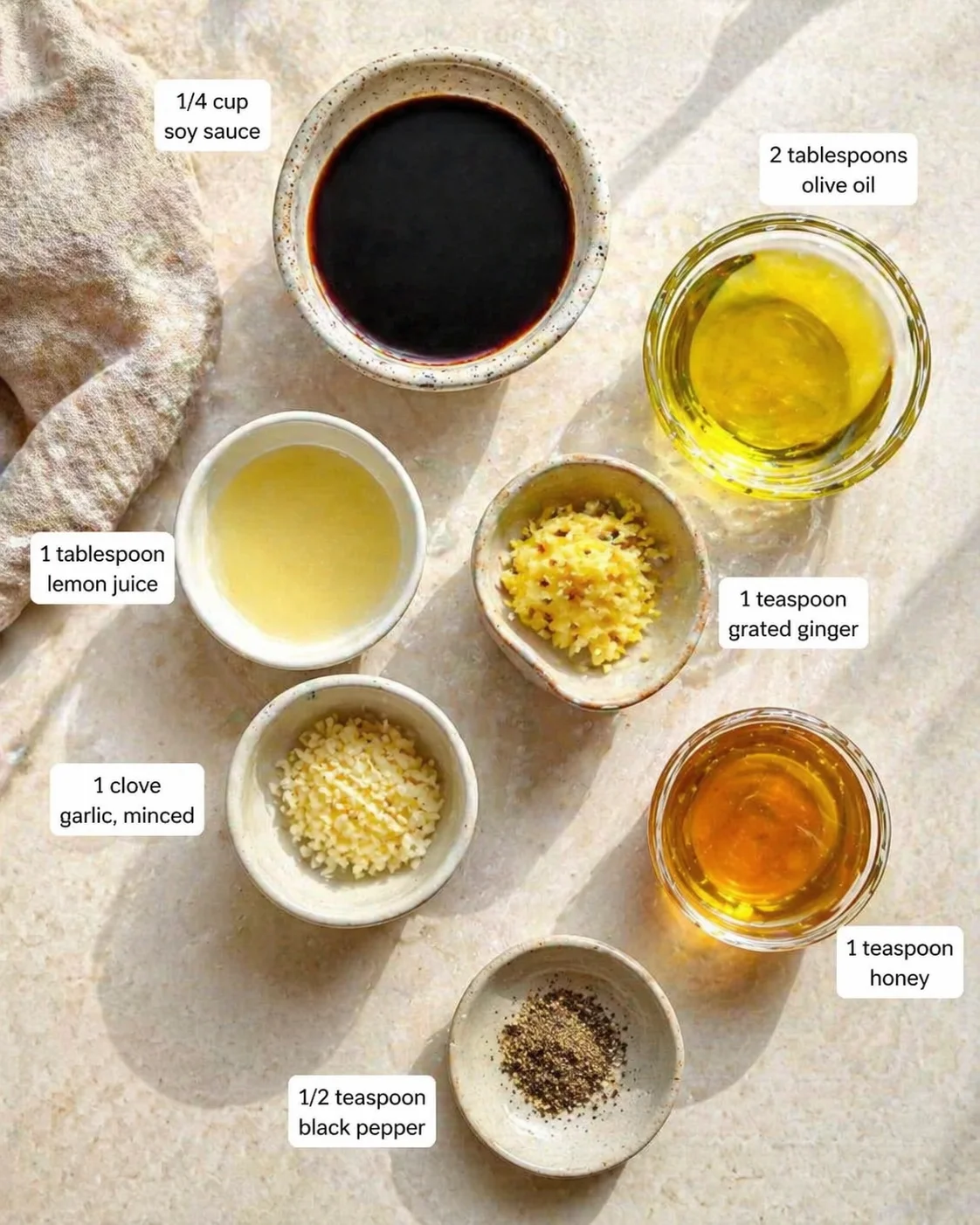 top-down view of ingredients for a marinade: soy sauce, olive oil, lemon juice, ginger, garlic, honey, pepper.