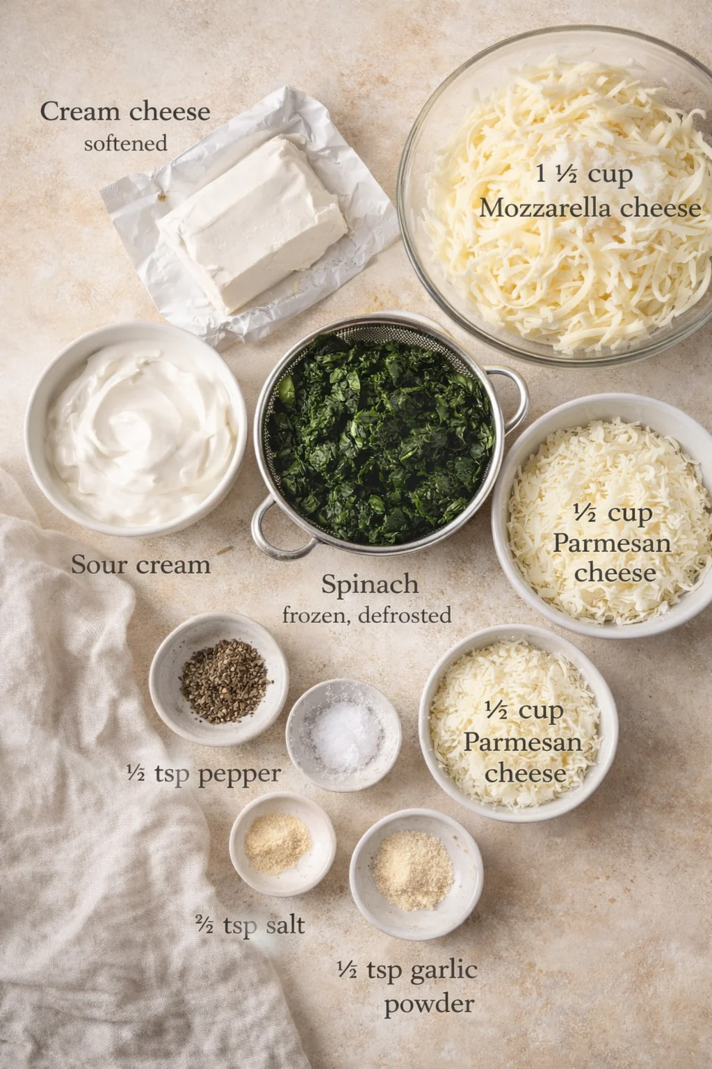 Overhead view of ingredients for spinach dip: cream cheese, sour cream, mozzarella, parmesan, spinach, and spices