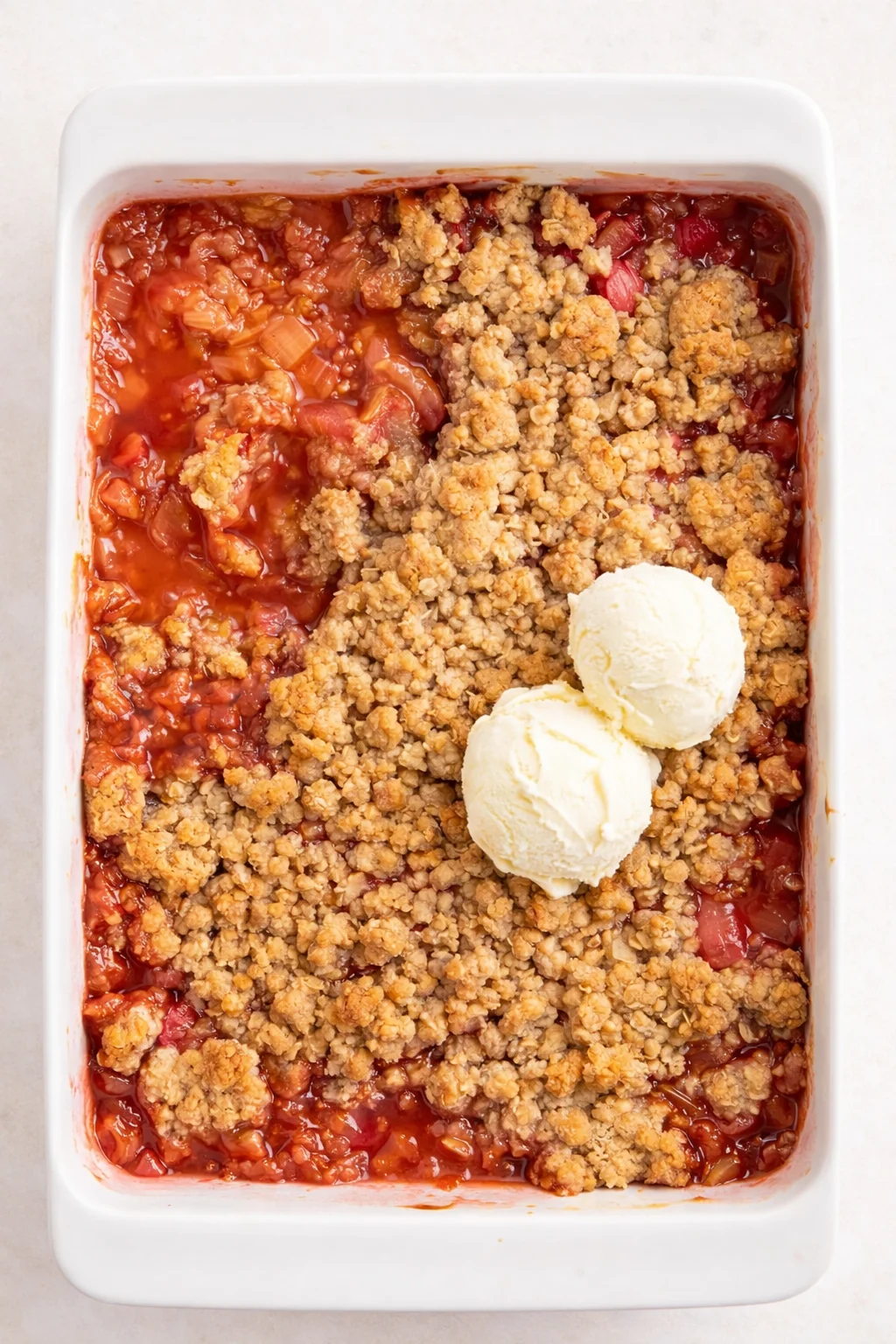 white rectangular baking dish with strawberry-rhubarb crumble and two scoops of vanilla ice cream
