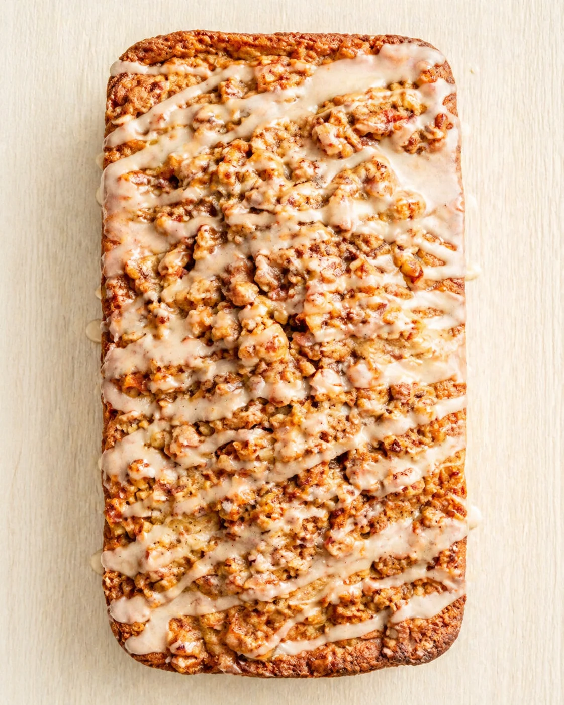 golden-brown streusel loaf with white glaze on light wooden surface