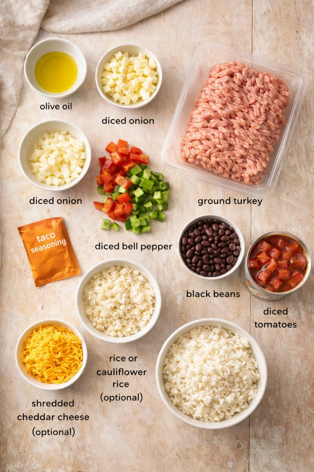 Overhead view of organized taco ingredients: ground turkey, onions, bell peppers, beans, tomatoes, rice, cheese, oil, and taco seasoning.