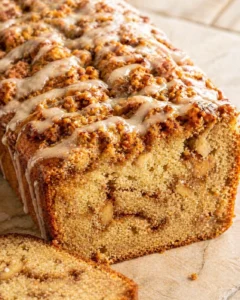 Close-up of a loaf cake with streusel topping and vanilla glaze, showing a moist interior.