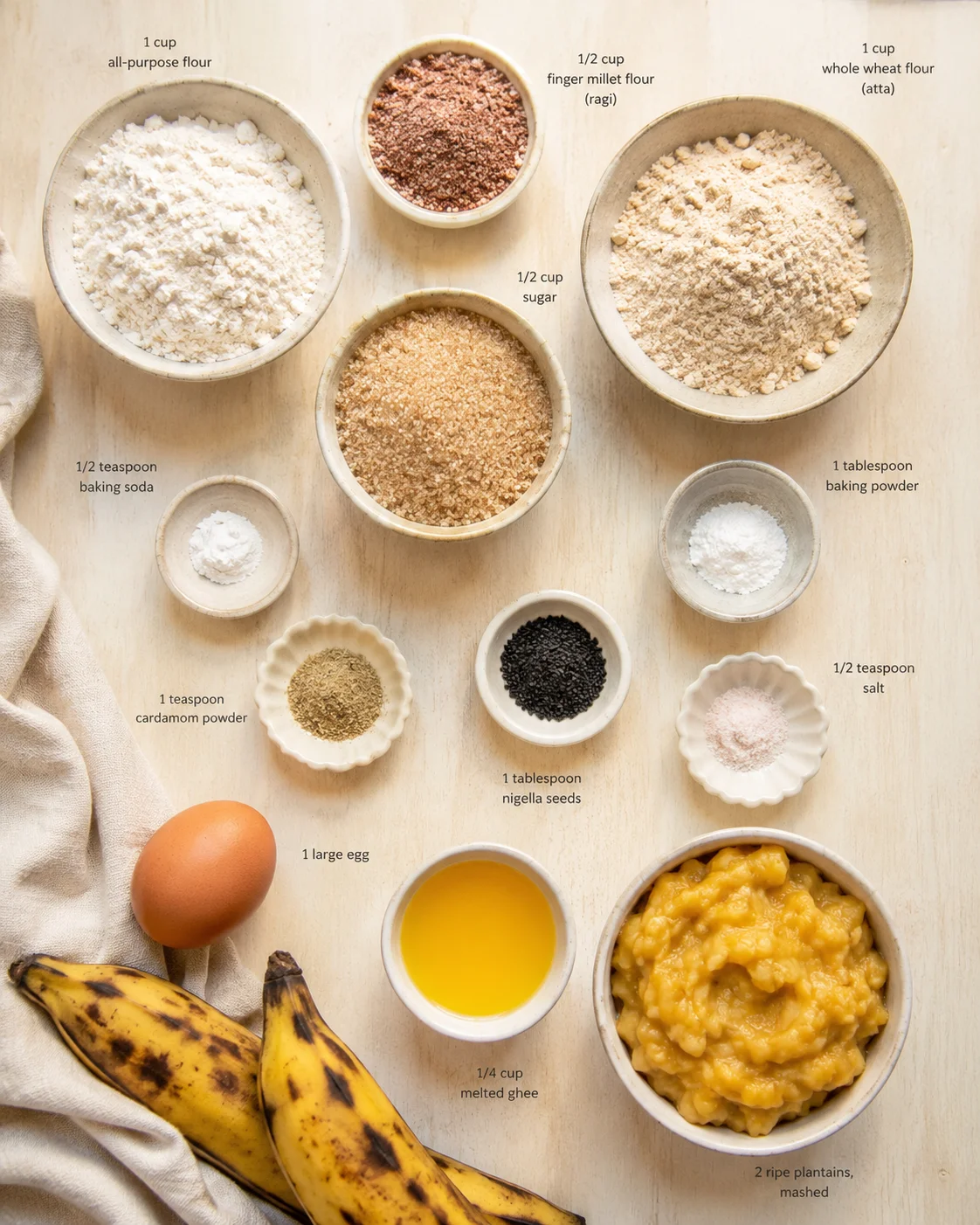 Overhead view of assorted baking ingredients arranged in labeled bowls on a light wooden surface.