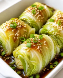 glazed cabbage rolls topped with sesame seeds and green onions in a savory sauce