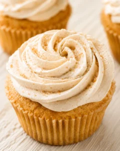 Close-up of a vanilla cupcake with swirled caramel-brown sugar frosting on a wooden surface.
