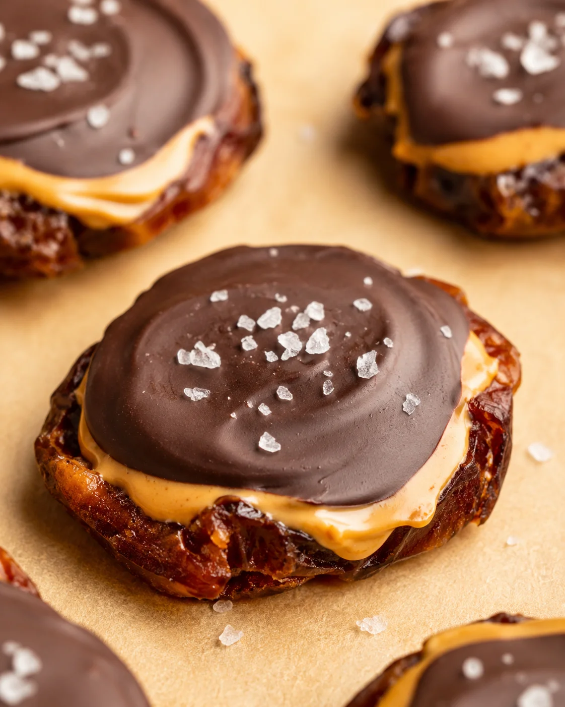 Close-up of chocolate-topped peanut butter bites with sea salt on parchment.