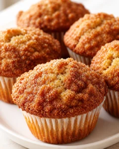 Close-up of golden-brown muffins with sugar-crystal tops on white liners