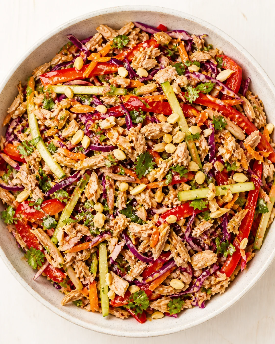 Bowl of colorful shredded chicken salad with red cabbage, bell peppers, carrots, cucumber, cilantro, and peanuts