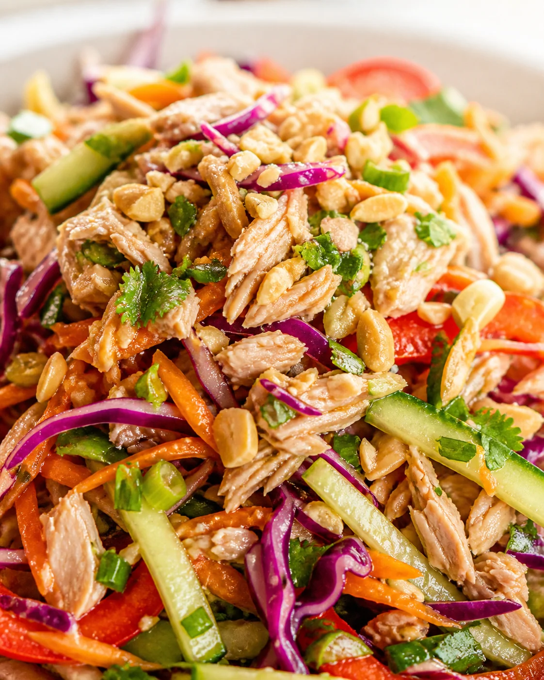 close-up of a colorful Thai-inspired chicken salad with shredded chicken, cucumbers, red onion, carrots, peanuts, and cilantro