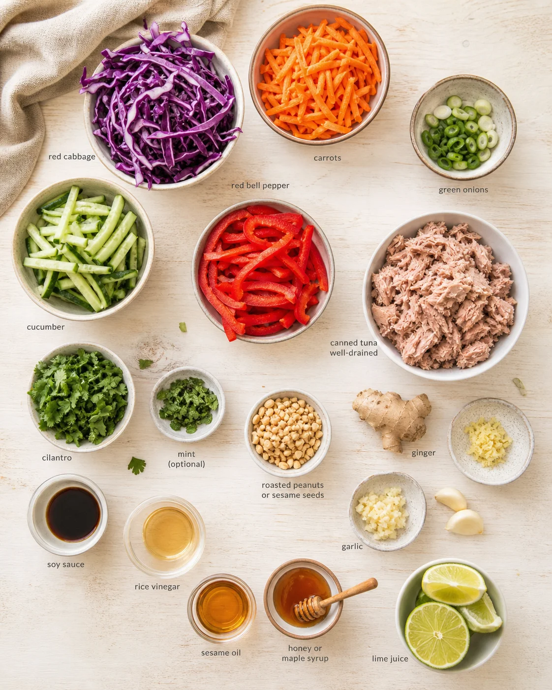 top-down view of bowls with red cabbage, carrots, cucumber, peppers, tuna, herbs, nuts, and condiments