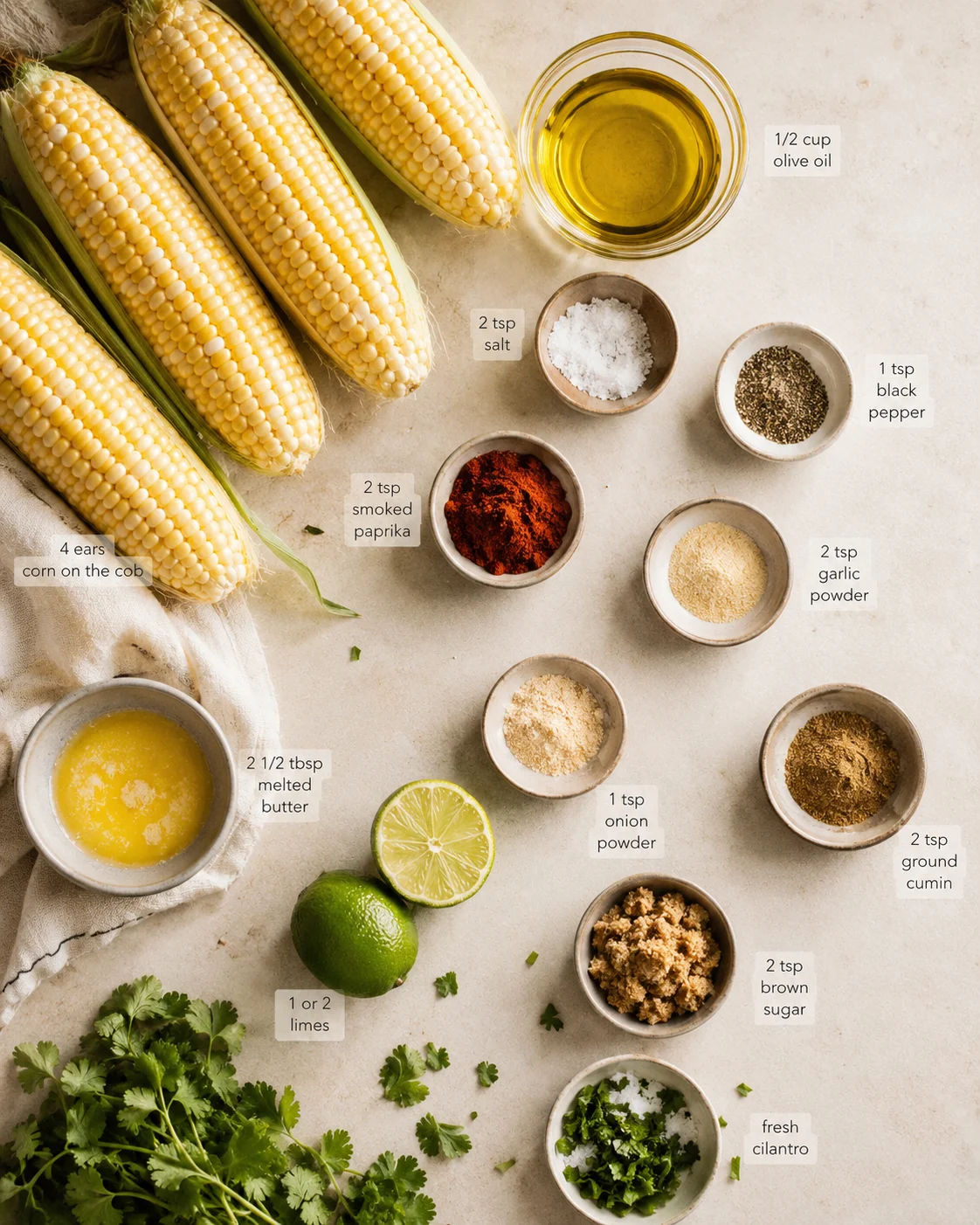 Flat lay of corn on the cob with spice bowls, oil, lime, butter, and cilantro