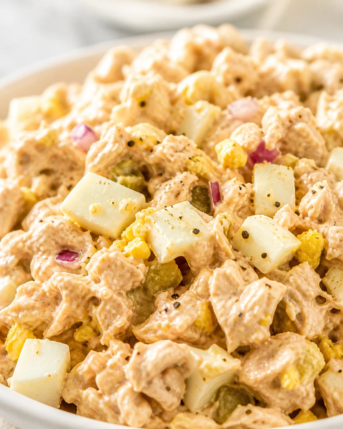 close-up of creamy chicken salad with potatoes, corn, red onion in a white bowl