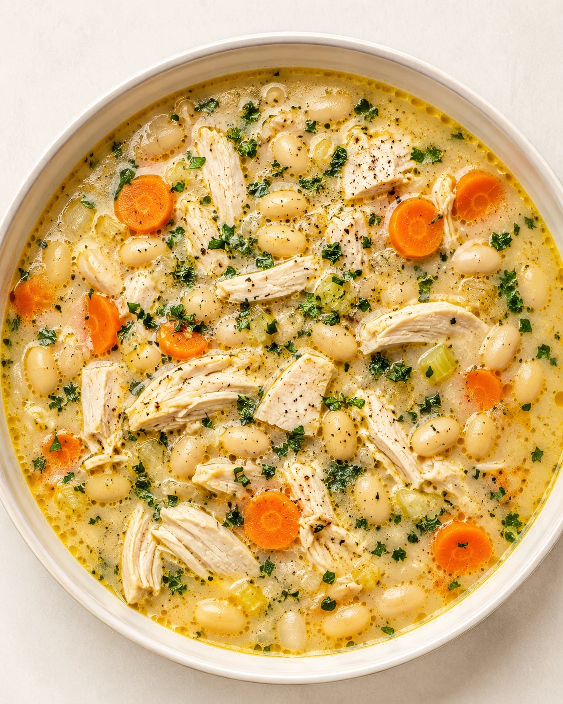 Creamy chicken and white bean soup with carrots, celery, and parsley in a pale broth.