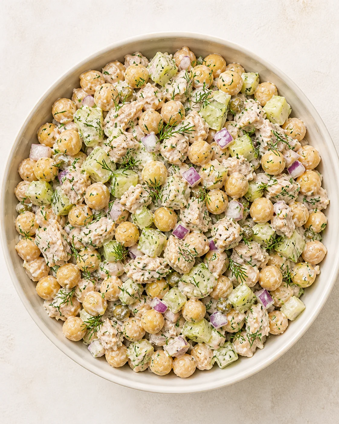 Overhead view of a creamy chickpea salad with cucumber, red onion and dill in a light bowl.