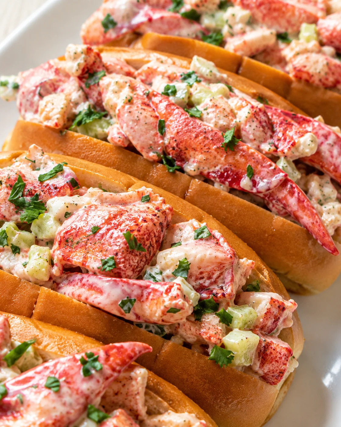 Lobster rolls with creamy mayo dressing, celery, and parsley on toasted buns.