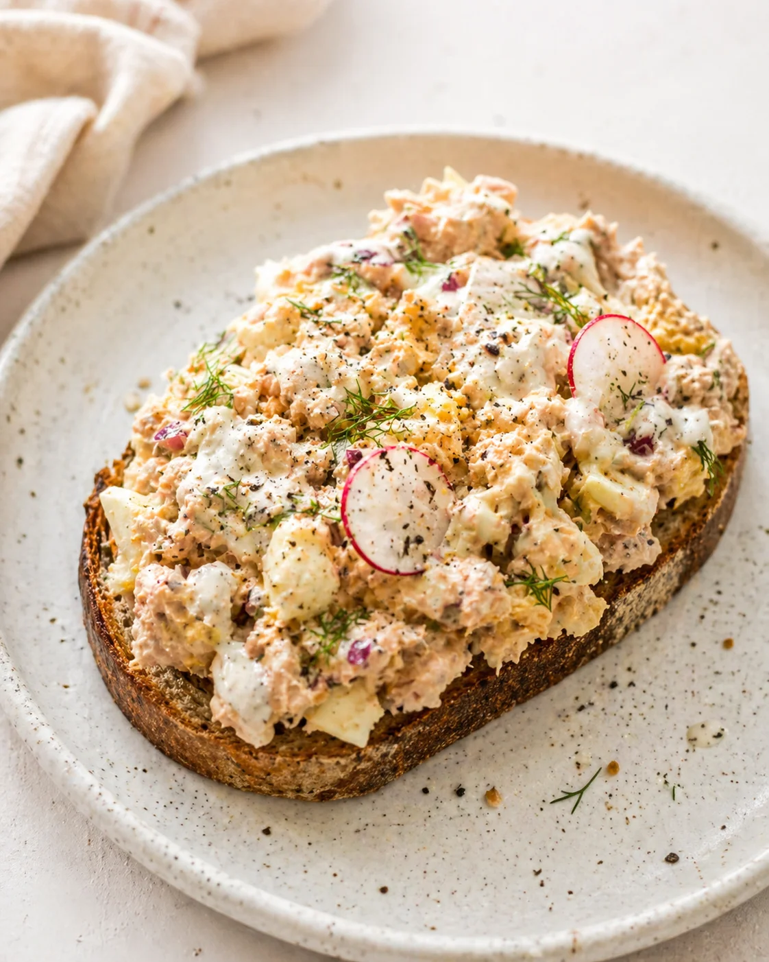 Sourdough toast topped with creamy potato salad, dill, and radish on a speckled plate.