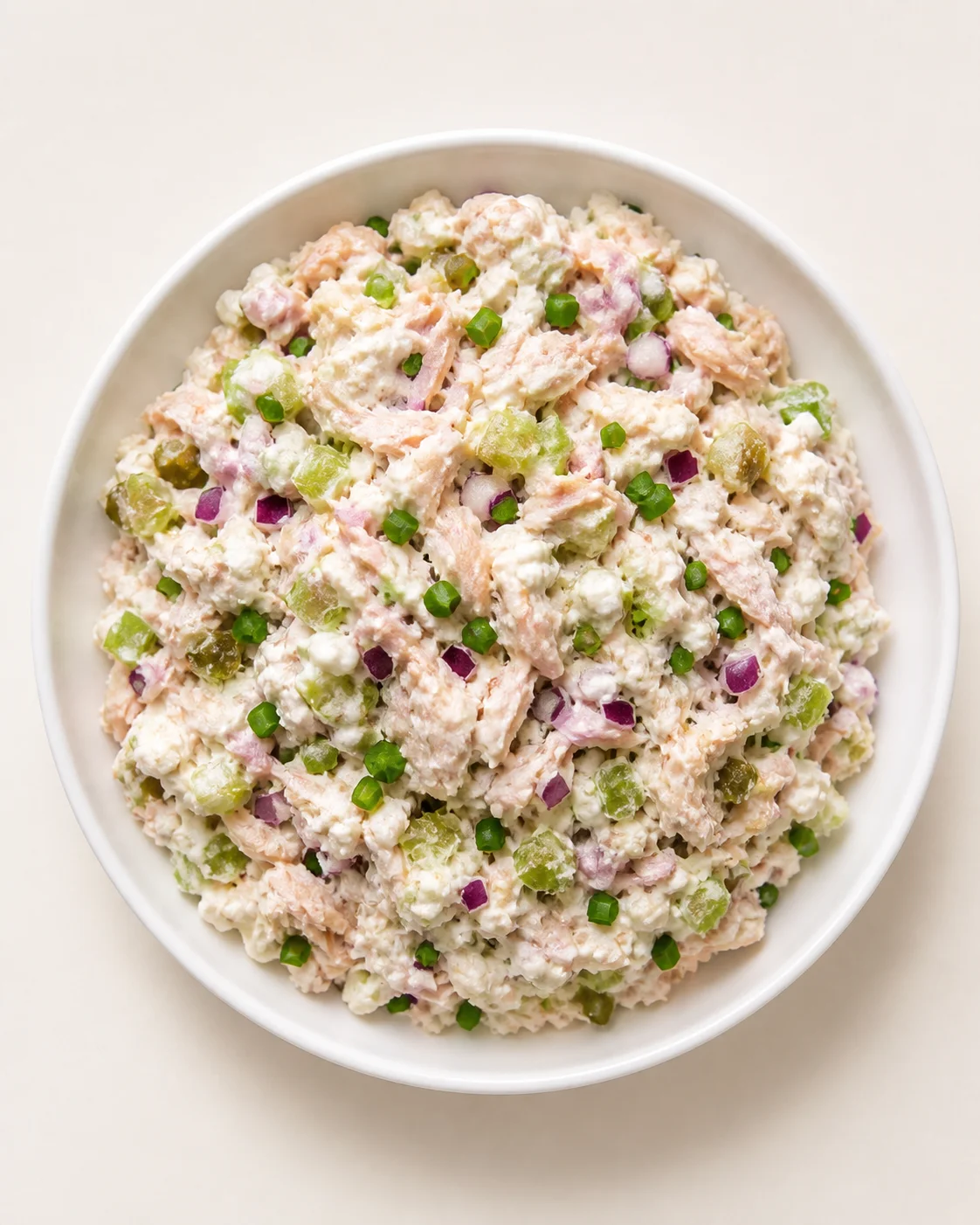 Creamy potato salad with diced celery, red onion, and green onions in a white bowl.