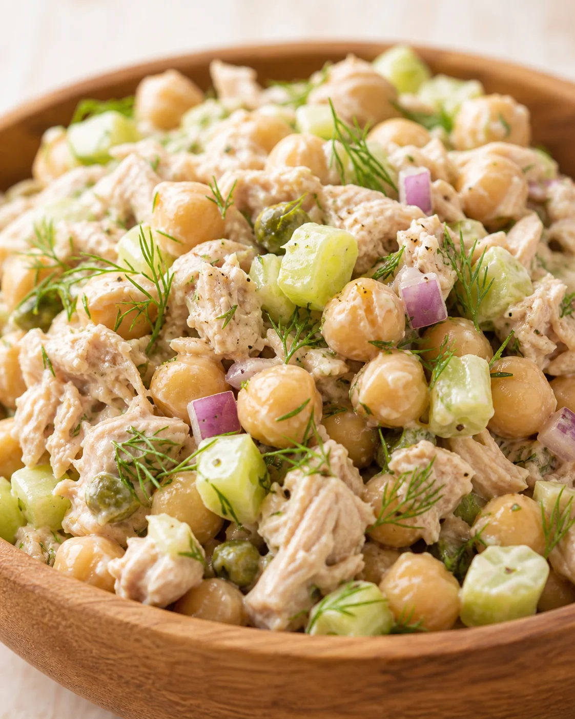 wooden bowl of creamy tuna chickpea salad with cucumber and dill garnish