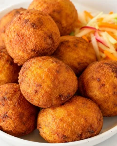 close-up of golden brown fried balls piled in a white bowl with colorful shredded slaw on the side