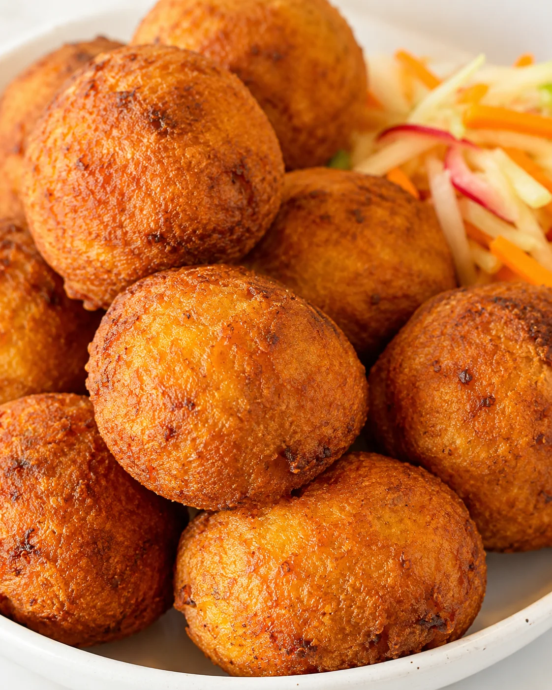 close-up of golden brown fried balls piled in a white bowl with colorful shredded slaw on the side