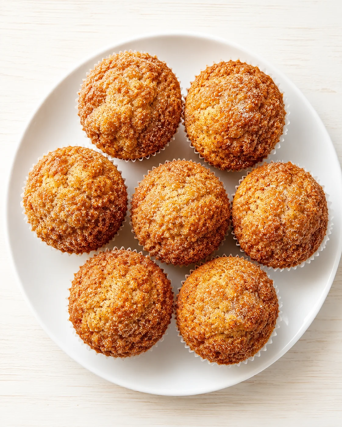 Top-down view of seven golden muffins with crumb topping arranged on a white plate.