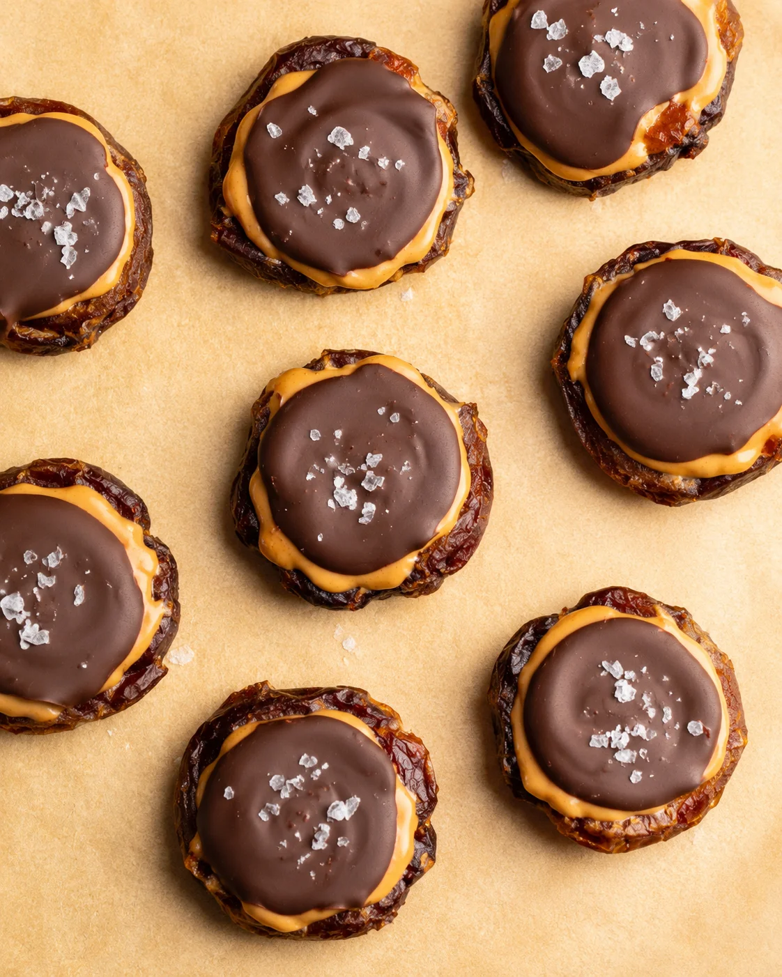 Top-down view of round chocolate-topped date bites with caramel centers on parchment.