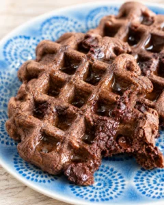close-up of fudgy chocolate waffles on a blue patterned plate with syrup drizzle