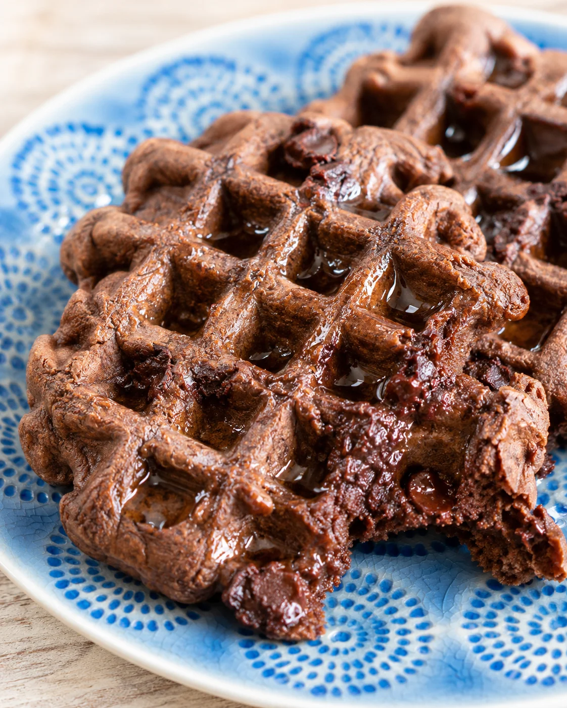 close-up of fudgy chocolate waffles on a blue patterned plate with syrup drizzle
