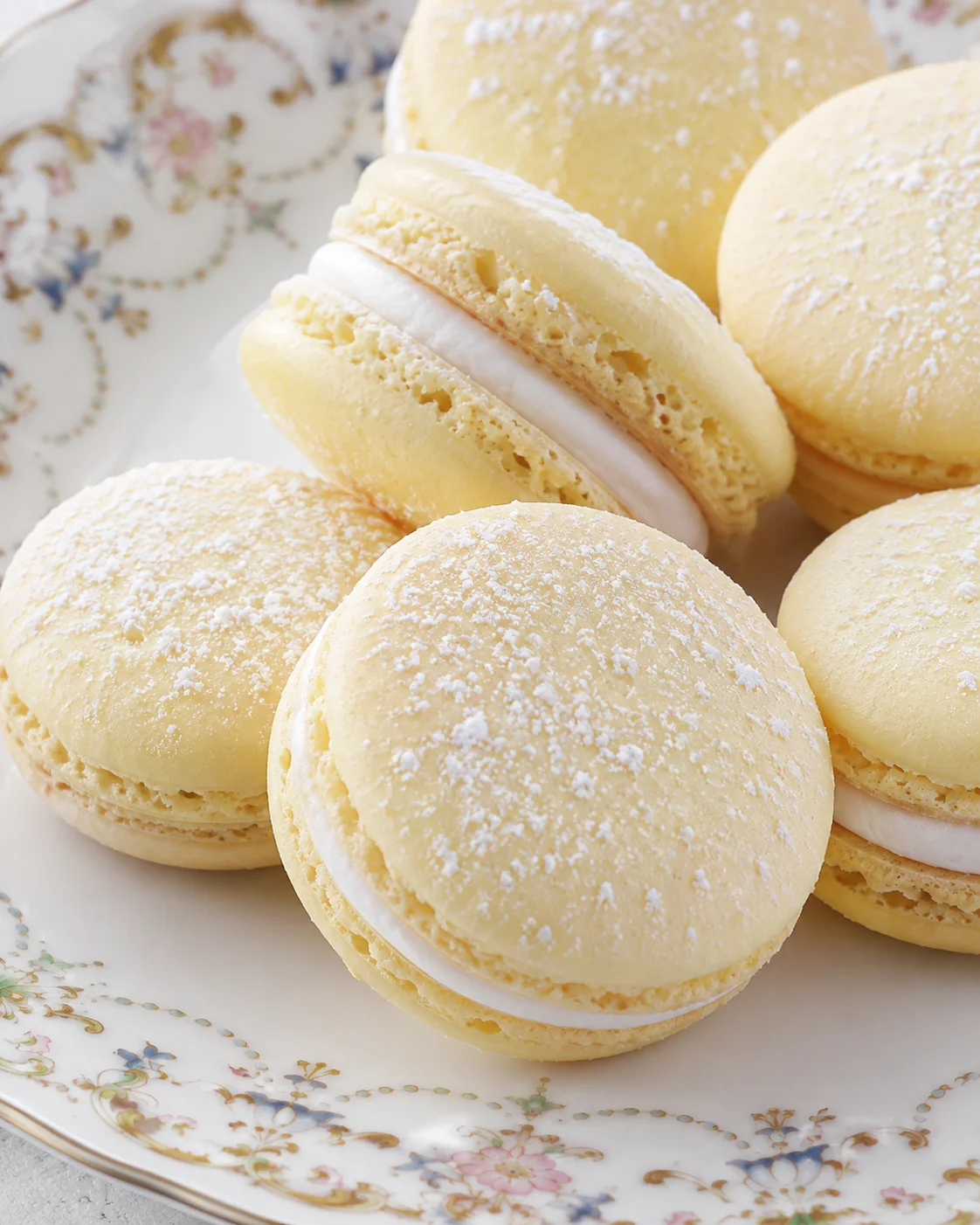 Close-up of pale yellow macarons with white filling on a floral-patterned plate.