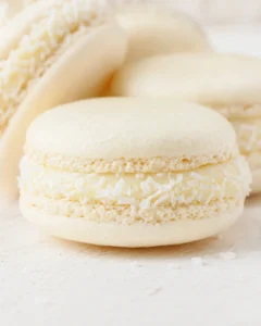 Close-up of ivory macarons with coconut-filled centers and coconut flakes on a light wooden surface