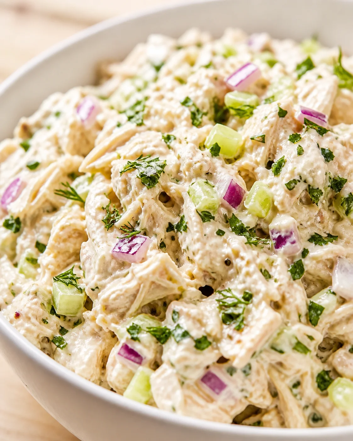 close-up of creamy chicken salad with red onion, celery, and dill in a white bowl.