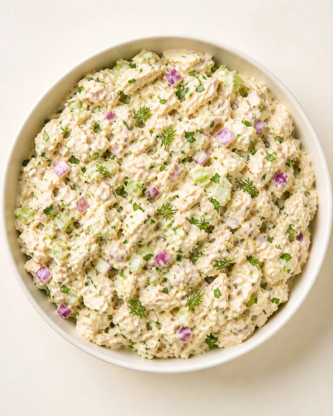 Creamy potato salad with diced red onions, celery, and fresh dill in a white serving bowl.