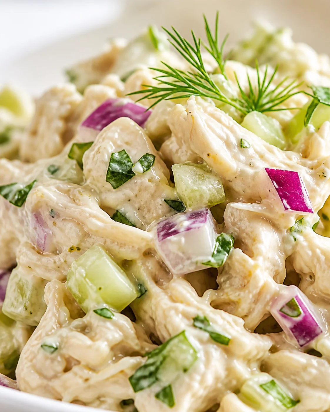 Close-up view of creamy potato salad with cucumber chunks, red onion, and dill garnish.
