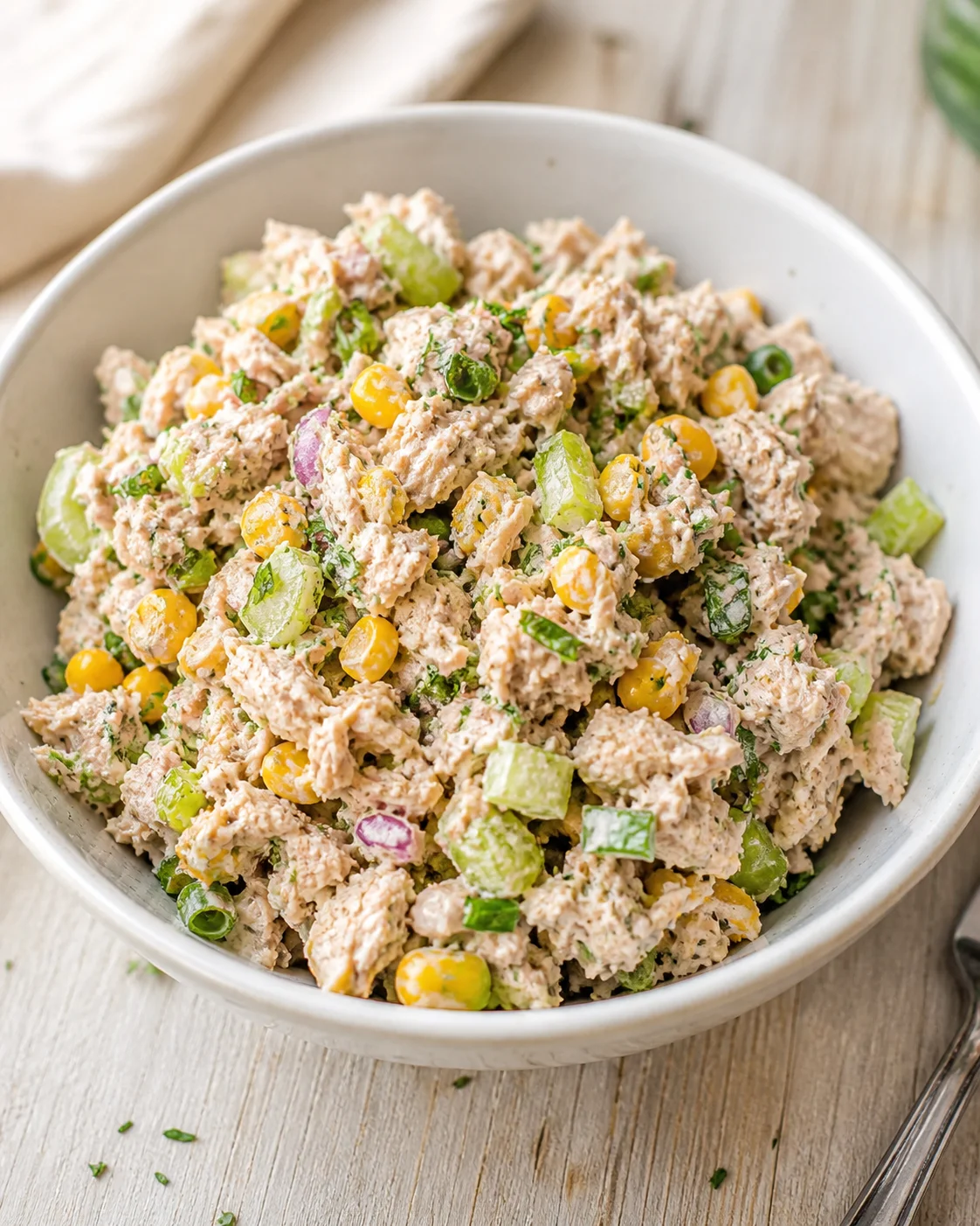 bowl of creamy tuna salad with corn, celery, red onion, and herbs on a wooden table