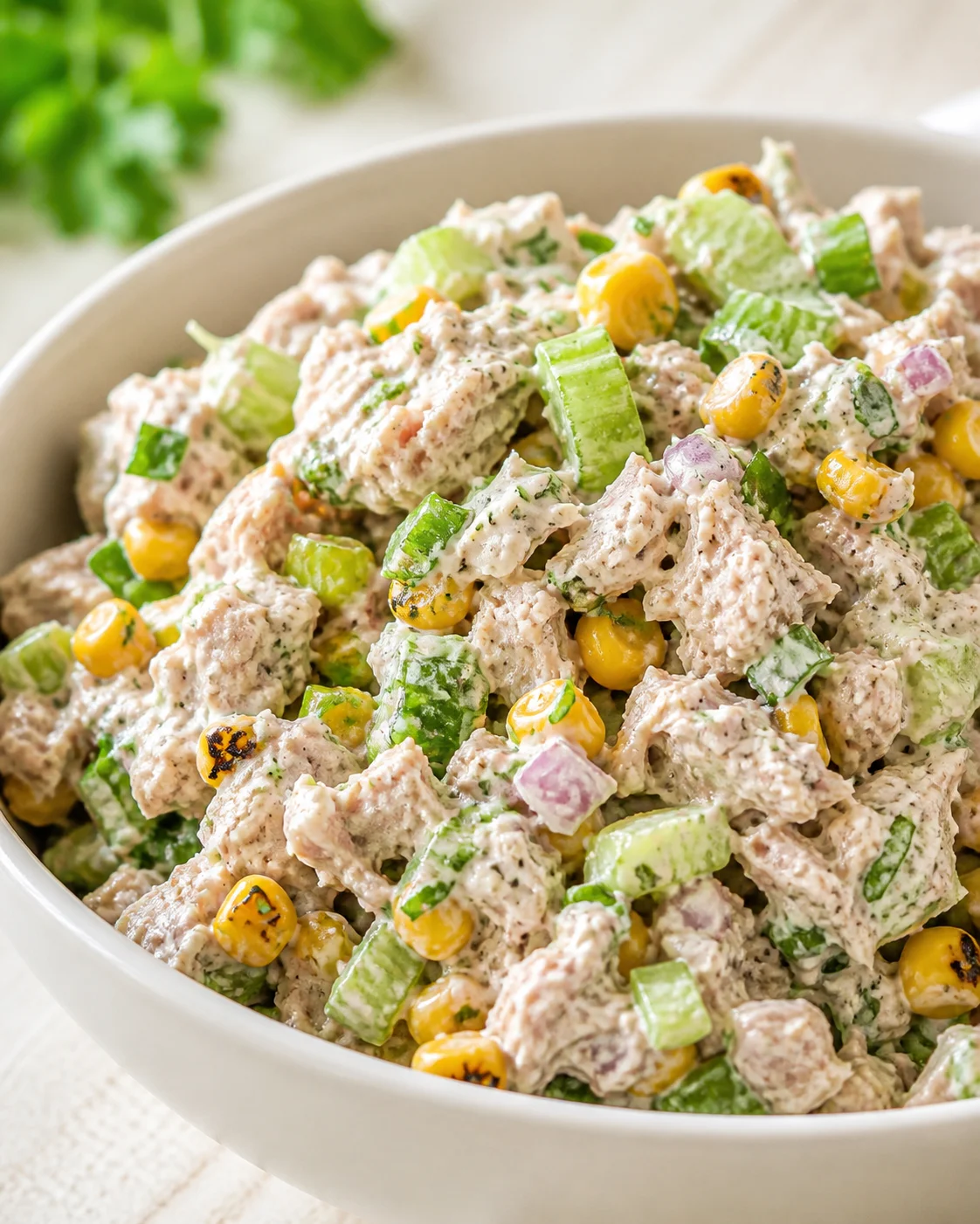 Close-up of creamy chicken salad with celery and corn in a white bowl.