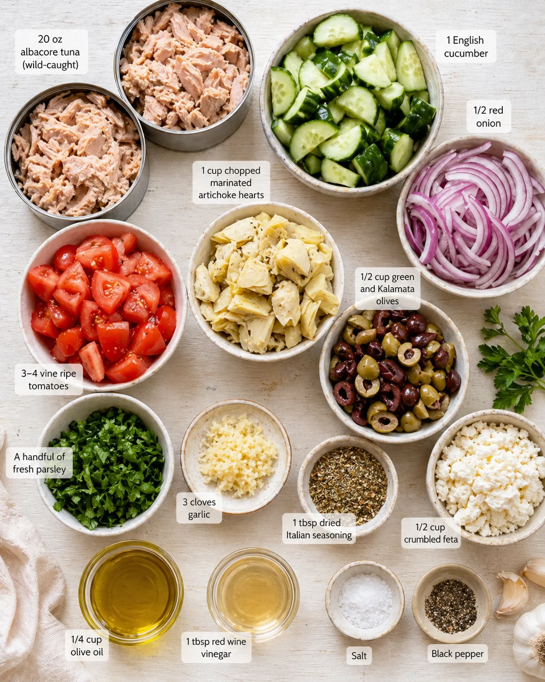 top-down view of labeled bowls with tuna, vegetables, olives, feta, and herbs.