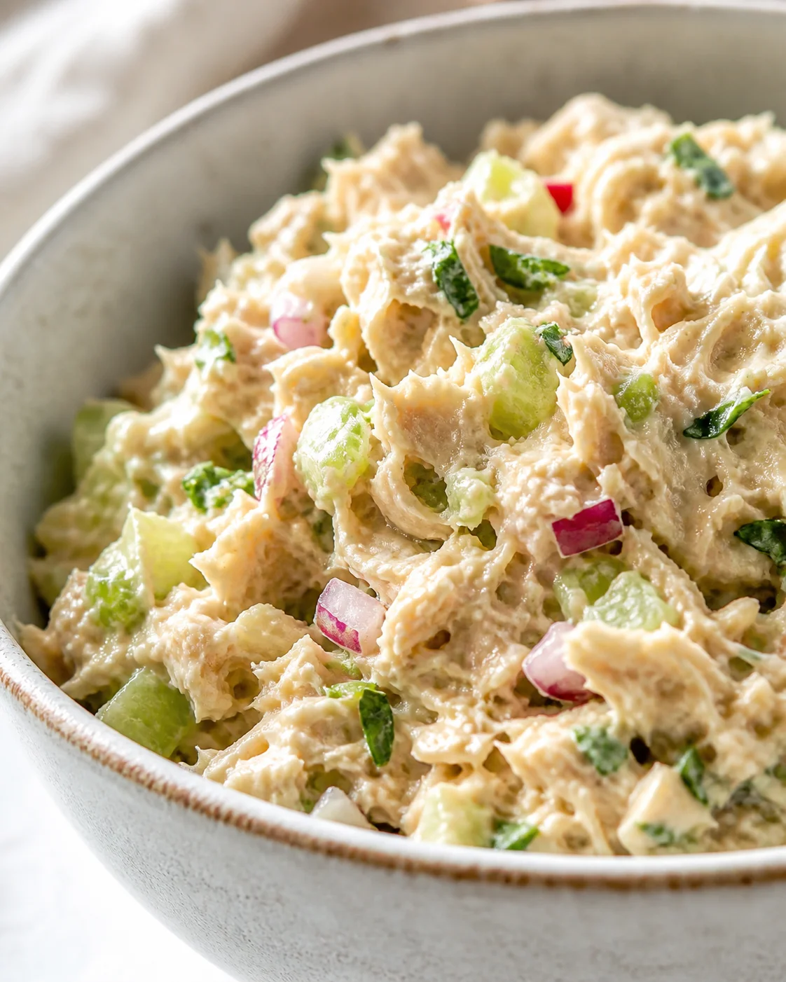 Creamy chicken salad with celery and red onion in a gray ceramic bowl