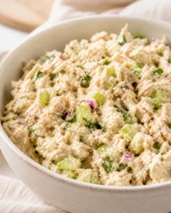 Creamy tuna salad with diced celery, red onion, and herbs in a beige bowl.