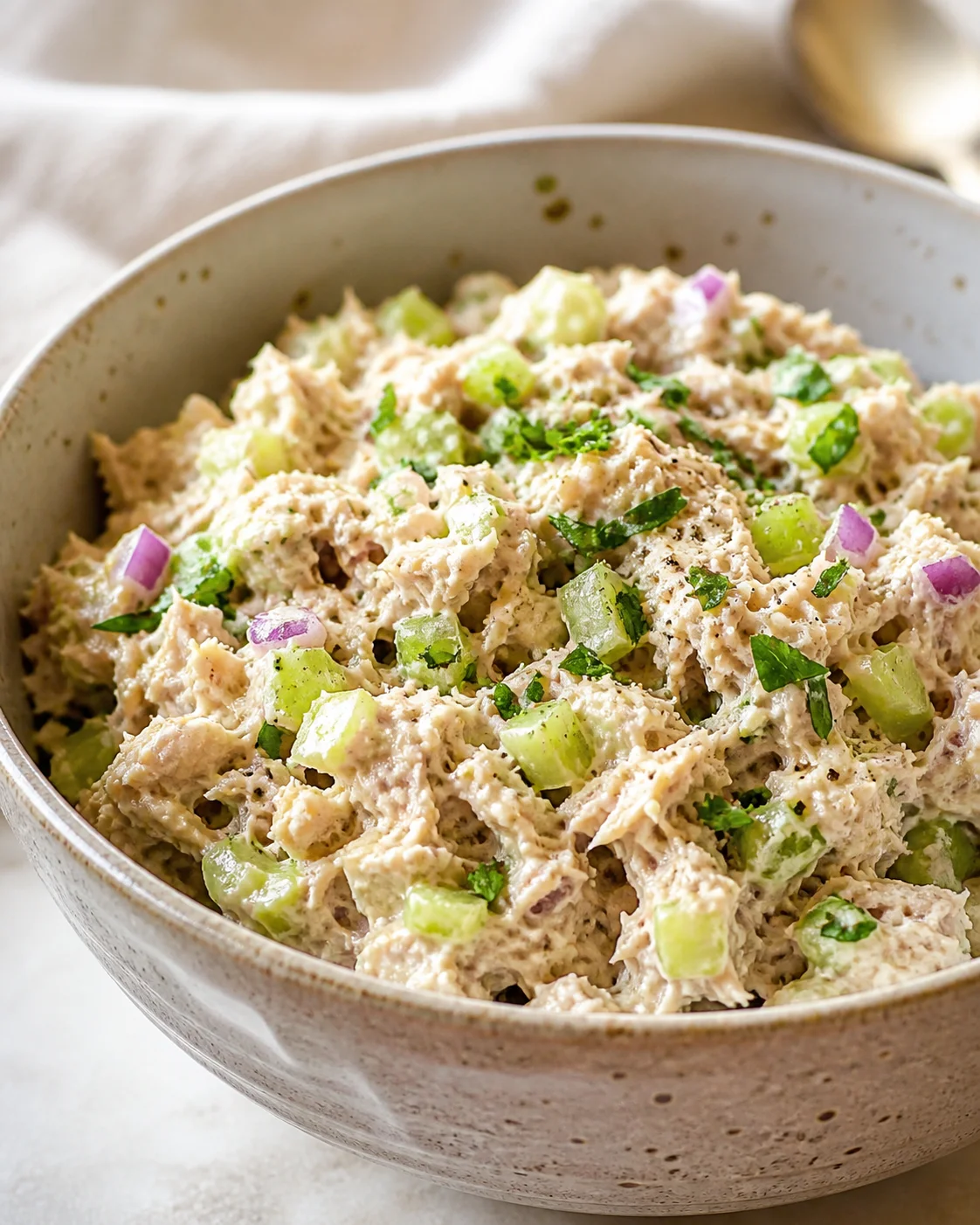 bowl of creamy chicken salad with celery and red onion garnished with herbs