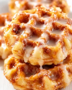 Close-up of glossy cinnamon rolls with creamy icing drizzling over a golden-brown stack.