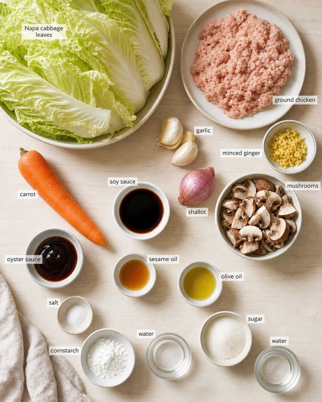Top-down view of napa cabbage and ground chicken with labeled ingredients arranged on a light wooden kitchen surface.