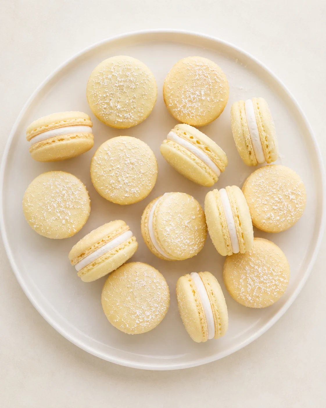 Pale-yellow macarons with white filling, dusted with sugar, arranged on a white plate.