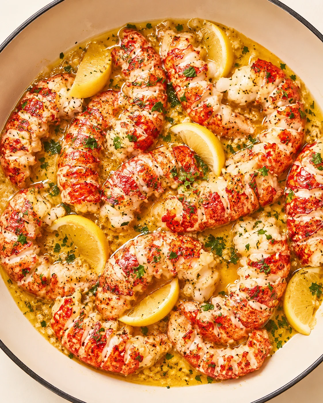 lobster tails in lemon-butter sauce with parsley in a white skillet